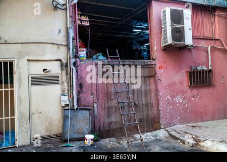 Eine hölzerne Leiter lehnt sich an einen abgenutzten rosafarbenen Lagereingang mit Klimaanlagen in einer verwitterten städtischen Hinterstraße in Istanbul, Türkei Stockfoto