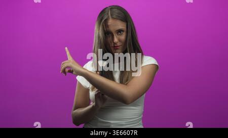 Frau junge Brünette trägt Make-up-Pinsel auf den Unterarm, während sie mit dem Finger in einem magentafarbenen Studio zeigt; Selbstbewusstsein. Stockfoto