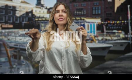 Frau, die eine Kreditkarte hält und mit dem Finger nach vorne zeigt, mit Booten am Hafen; Selbstvertrauen stärken. Stockfoto
