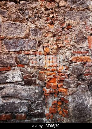 Verwitterte und alte strukturierte Steinmauer mit freiliegenden roten Ziegeln und rauen Mörtelfugen, die historische Architektur zeigen Stockfoto