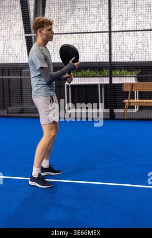 Männlicher Athlet, der auf dem Padel-Platz in der Sportanlage steht, Schläger in der Nähe der weißen Linie und des Netzes hält Stockfoto