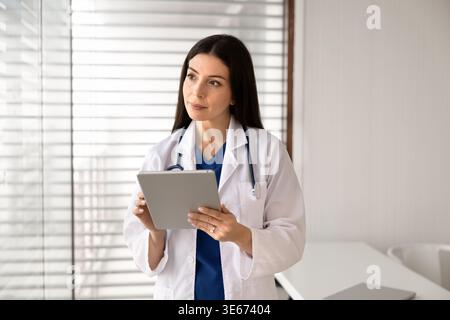 Fokussierter Arzt, der an einem digitalen Tablet arbeitet, steht in der Klinik Stockfoto