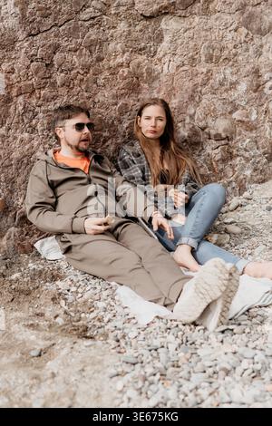 Paare Strandentspannung junger Mann und Frau, die während eines Sommerurlaubs zusammen an einer Felsmauer an einem Kieselstrand sitzen Stockfoto