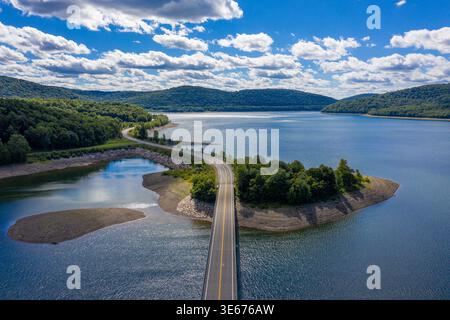 Aus der Vogelperspektive auf die gewundene Straße, die den See mit bewaldeten Hügeln und blauem Himmel im Norden von New York überquert Stockfoto