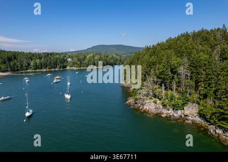 Blick aus der Vogelperspektive auf den Küstenhafen in der Nähe des Acadia-Nationalparks in Maine mit Segelbooten, die in ruhigem Wasser verankert sind und von einer bewaldeten Küste umgeben sind Stockfoto