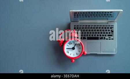 Hochwinkelansicht eines roten Weckers auf einem Miniatur-Laptop, der Termine für die Fernarbeit und Zeitmanagement für digitale Nomaden darstellt. Stockfoto