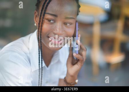 Nahaufnahme eines Porträts einer jungen Schwarzen Frau, die mit einem warmen Lächeln auf dem Smartphone zuhört. Freundliche Unterhaltung, Mobiltechnologie, Kundenservice, persönlich Stockfoto