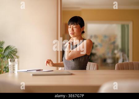 Junge Geschäftsfrau mit geschlossenen Augen, die Rückenschmerzen durch längeres Sitzen beim Arbeiten am Schreibtisch im Büro hat Stockfoto