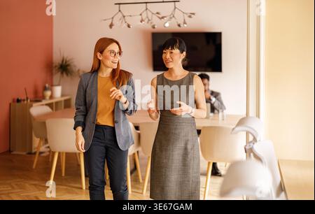 Verschiedene professionelle Kollegen sprechen und arbeiten zusammen, während sie an einem modernen Büroarbeitsplatz gemeinsam laufen Stockfoto