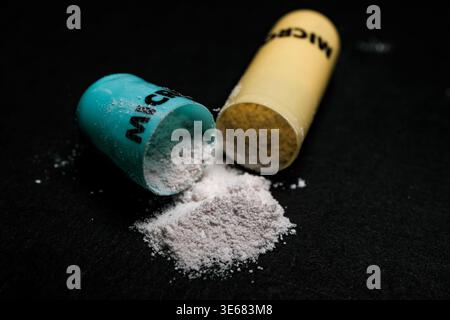 Zwei geöffnete Kapselhälften verschütten feines weißes Pulver auf eine dunkle Oberfläche, eine Nahaufnahme mit dramatischer Beleuchtung Stockfoto