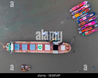 Ein hochwinkliger Drohnenschuss, der direkt auf einen großen Massengutfrachter und mehrere kleinere Lastkähne blickt, die mit lebhaften, farbenfrohen Schiffscontainern beladen sind. Th Stockfoto