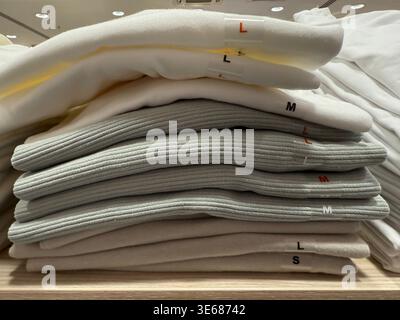 Gefaltete Pullover stapeln sich auf einem Holzregal mit Größenetiketten in einem Bekleidungsgeschäft. Mobiles Foto Stockfoto