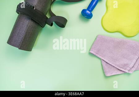 Flache Aufstellung von Fitnessaccessoires einschließlich Kurzhanteln, Handtuch, Yogamatte auf grünem Hintergrund. Ideal für Fitness- und Gesundheitskonzepte. Stockfoto