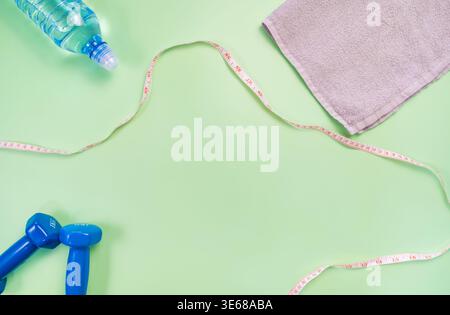 Flaches Anlegen von Fitnessaccessoires einschließlich blauer Kurzhanteln, Handtuch, Wasserflasche, Maßband auf grünem Hintergrund. Stockfoto