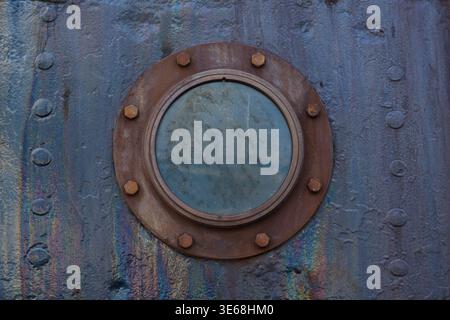 Nahaufnahme eines rostigen Bullauchs auf einem alten Metallschiffrumpf. Industrieller Hintergrund mit rundem Fenster und verwitterter Metalloberfläche. Stockfoto