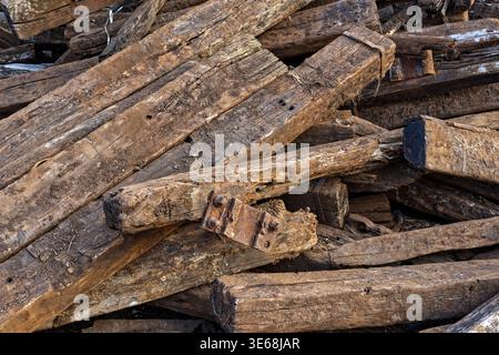 Eine Nahaufnahme eines unordentlichen Haufens von wiedergewonnenen hölzernen Bahnschwellen. Die Textur zeigt gereiftes, verrottendes Holz mit Rissen, Schmutz und Rost Stockfoto