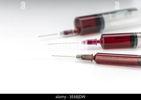 Nahaufnahme von drei mit Blut gefüllten medizinischen Spritzen, die nur zum einmaligen Gebrauch gekennzeichnet sind, mit scharfen exponierten hypodermischen Nadeln unterschiedlicher Größe, arran Stockfoto