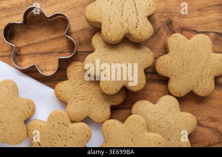Blick von oben auf frisch gebackene Weihnachtskekse mit Metallkeksschneider auf rustikaler Holzoberfläche. Festliches Backen und Urlaubsvorbereitung Stockfoto