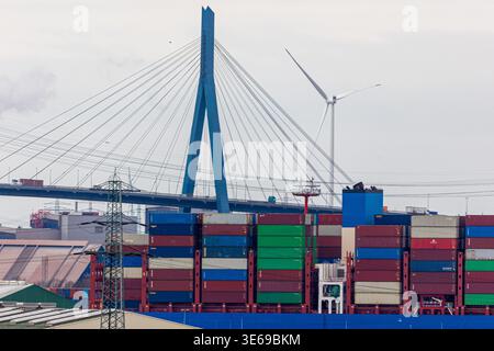 Containerschiff beladen mit bunten Frachtcontainern, das durch den belebten Industriehafen Hamburg fährt. Deutschland. Mit der ikonischen Köhlbrand-Brücke A Stockfoto