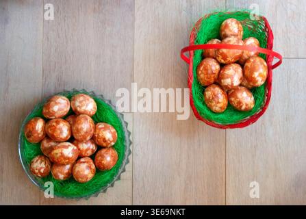 Natürlich gefärbte Ostereier in Glasschale und Korb schräg auf rustikalem Holzhintergrund mit Kopierraum platziert. Traditionelle Urlaubskomposition Stockfoto