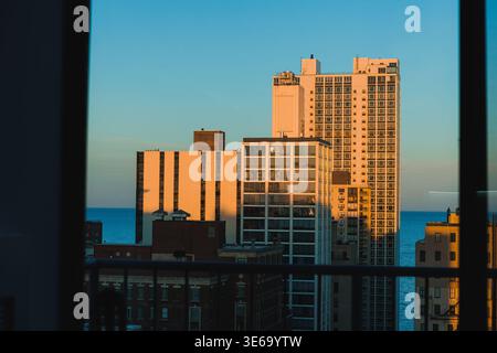 Die Sonne untergeht über Chicago und wirft warmes Licht auf hohe Gebäude. Die Aussicht zeigt eine Mischung von Strukturen in der Nähe des Wassers, die in der Abenddämmerung eine Skyline der Stadt bilden. Stockfoto