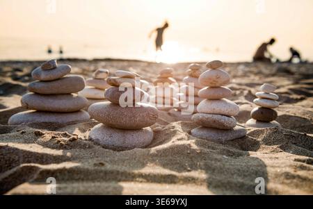 Zen-Steintürme stapelten sich bei Sonnenuntergang auf dem Sand des Strandes Agios Gordis. Ausgeglichene Kieselsteine an der Küste von Korfu, Griechenland, aufgenommen am 12. Juli 2023. Stockfoto