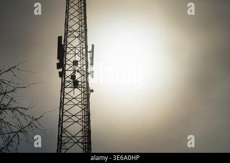 Industrieller Kommunikationsmast und Mobilfunksender stehen hoch in einem dichten Morgennebel, während die Sonne durch dicken Nebel in einem urba leuchtet Stockfoto