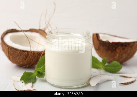 Köstlicher Kokosjoghurt im Glas, Hälften Obst, Flocken und Minze auf dem Lichttisch, Nahaufnahme Stockfoto