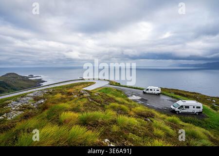 Zwei weiße Wohnmobile parkten an einer spektakulären malerischen Kurve in Kråkenes, Norwegen. Die Küstenstraße überblickt den Atlantik unter einem dramatischen Himmel, su Stockfoto