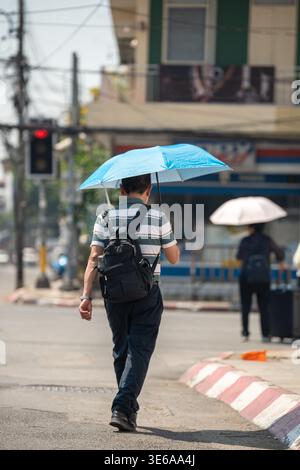 Mann, der durch die Stadt geht und einen Schirm hält, Gesundheitssicherheit und Schutz vor Hitzschlag bei Hitzewellen. Stockfoto