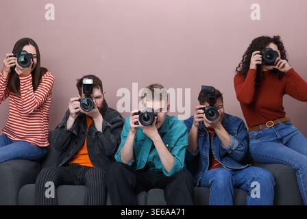 Gruppe von Fotografen, die Fotos mit professionellen Kameras auf Sofa vor farbigem Hintergrund machen Stockfoto