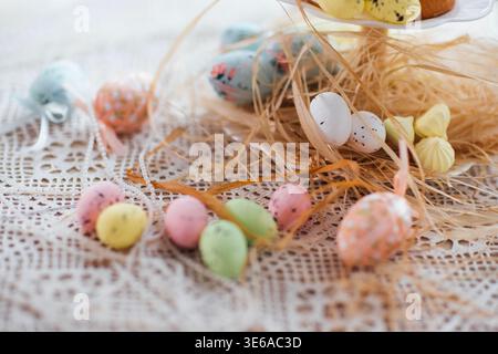Dekorative Ostereier in verschiedenen Pastellfarben sind auf einer Tischdecke mit Strohhalm verstreut und unterstreichen das festliche Frühlingsthema für Feiertage Stockfoto