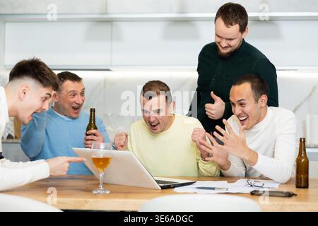 Eine Gruppe von Freunden, die gemeinsam ein Fußballspiel auf einem Laptop anschauen und Bier trinken Stockfoto