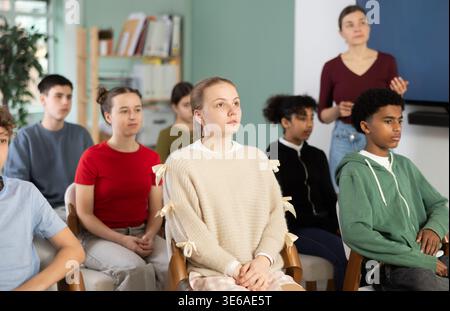 Während des Treffens in der Klasse hören die Teenager-Schülerinnen Vorlesungen, weibliche Lehrerin im Hintergrund. Stockfoto