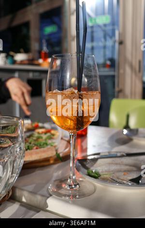 Während einer Mahlzeit steht ein Getränk in einem Glas auf dem Tisch. Es gibt Teller mit Essen und die Leute genießen ihre gemeinsame Zeit in einem Restaurant. Stockfoto