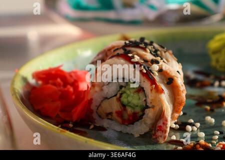 Sushi-Brötchen werden während des Mittagessens zusammen mit Wasabi und eingelegtem Ingwer in einem Restaurant auf eine grüne Platte gelegt, die verschiedene Zutaten und Farben zeigt. Stockfoto