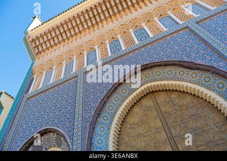 Niedrigwinkelaufnahme des Königlichen Palastes von Fès in Marokko mit lebendigen Zelij-Mosaikfliesen, komplizierten Gipsschnitzereien und einer massiven goldenen Messingtür Stockfoto