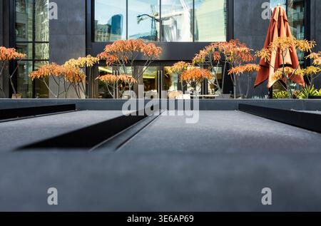 Vor einem Gebäude mit großem Fenster befindet sich ein schwarz-orangefarbener Schirm. Der Schirm ist offen und die Blätter sind orange. Innenhof zur Begrüßung. Stockfoto
