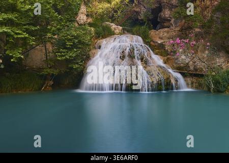 Ein kleiner Wasserfall fließt in einen ruhigen türkisblauen Pool, umgeben von Blumen und Felsen, Wasserfällen, Teichen, Polylimnio, Peloponnes, Griechenland Stockfoto