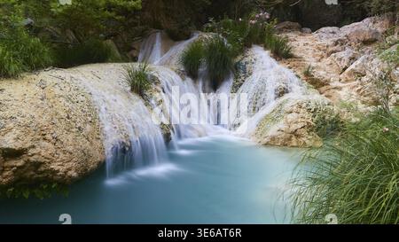 Ein kleiner Wasserfall fließt über Felsen in einen klaren türkisblauen Pool, der von Pflanzen, Wasserfällen, Teichen, Polylimnio, Peloponnes, Griechenland Stockfoto