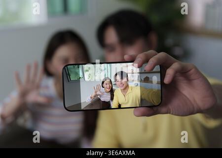 Ein Mann und eine Frau lächeln und winken in die Kamera, während sie ein Selfie machen und einen Moment voller Spaß und Verbundenheit festhalten Stockfoto