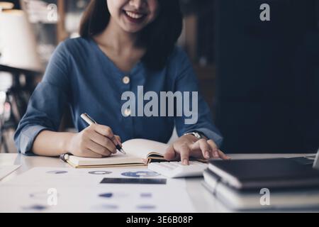 Asiatische Geschäftsfrau oder Buchhalterin Hände halten Stift in Notizbuch mit Papierkram, Konto, Audit und Sparkonzept Stockfoto
