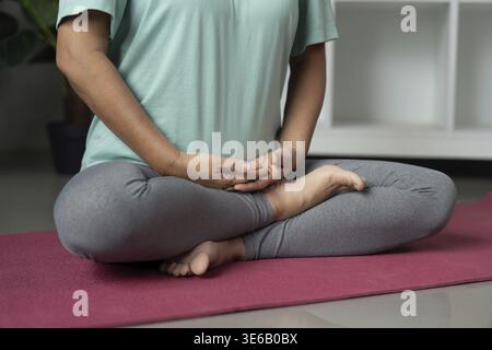 Konzentrierte ältere Frau, die in einer meditativen Haltung auf einer Yogamatte sitzt und Achtsamkeit und Entspannung in einer beruhigenden Innenumgebung übt Stockfoto