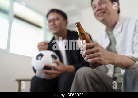 Zwei Männer jubeln ihrem Lieblingsfußballteam bei einem Drink in einem gemütlichen Wohnzimmer zu Stockfoto