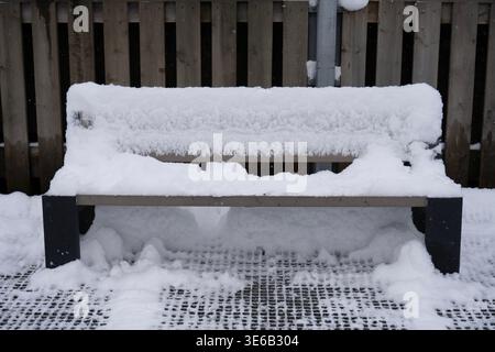 Eine ruhige Winterszene in Tromsø, Norwegen, zeigt eine schneebedeckte Bank, die unter einem sanften Schneefall ruht. Dicke Schichten von Neuschnee bedecken den Sitz. Stockfoto