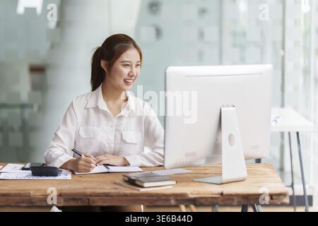Schöne asiatische Geschäftsfrau, die sich ein informatives Webinar am Computer ansieht. Finanzierungskonzept Stockfoto