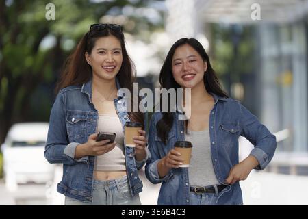 Zwei junge Frauen lächeln und halten Kaffeetassen in der Hand, während sie draußen laufen und Freundschaft und Verbindung feiern. Perfekt für Lifestyle-Themen Stockfoto