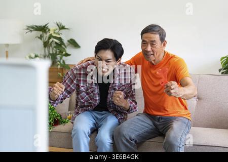 Ein Großvater und ein Enkel teilen die Begeisterung, während sie ein Sportspiel im Fernsehen ansehen und Familienbeziehungen zeigen Stockfoto