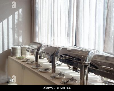 Frühstücksbüfett im Resort-Hotel mit Scheuergerichten aus Edelstahl, Tellern und Servierlöffeln auf einem langen Tisch. Konzept der Gastfreundschaft Stockfoto