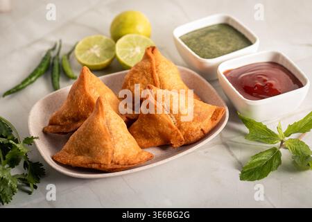 Knusprige goldene Samosa serviert mit Minz-Chutney-Tomatensoße frische Zitrone auf Holzbrett indischer Street Food Snack köstliche Vorspeise Stockfoto
